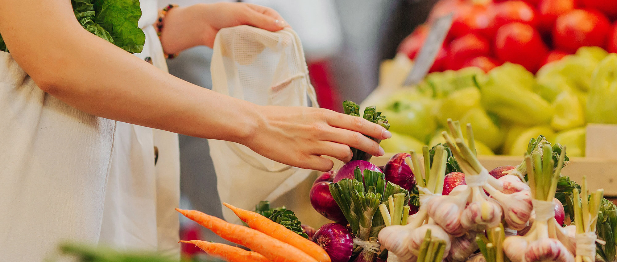 A woman chooses produce at a produce stand. Her face is unseen.
