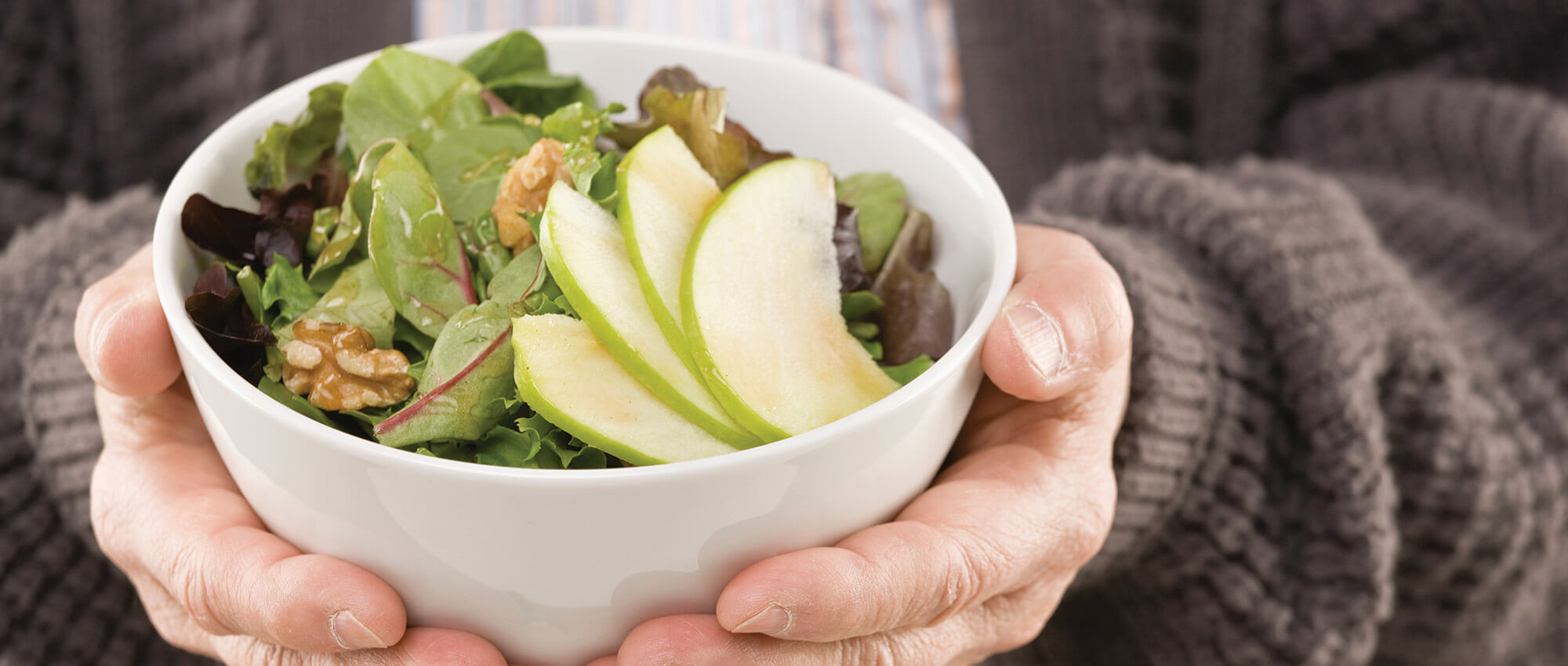 Two hands of an unseen person holding a salad in a white bowl.